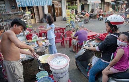 Một quầy bán hàng di động tại quận Tân Bình, thành phố Hồ Chí Minh với bàn ghế nhựa nhẹ tênh giúp người bán bánh tráng này có được địa điểm bán hàng lý tưởng. Người Việt Nam càng lúc càng bận rộn và yêu cầu tốc độ, này là người mẹ đèo con tấp vội vào mua bánh, kia là cậu bé học sinh tranh thủ táp vào ăn món quà vặt.